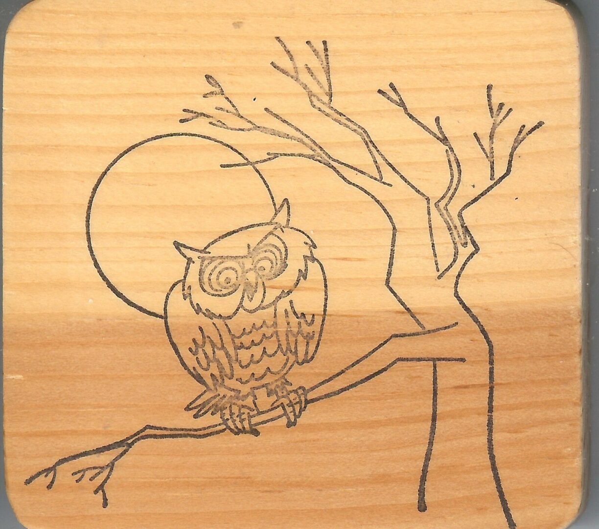 A wooden picture of an owl sitting on a tree branch.
